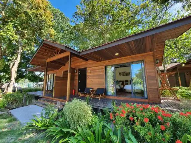 Timber beach chalet with a glazed front and a terrace among red flowers and trees at Borneo Divers Mabul Resort (placeholder, to recheck when the photo is replaced)